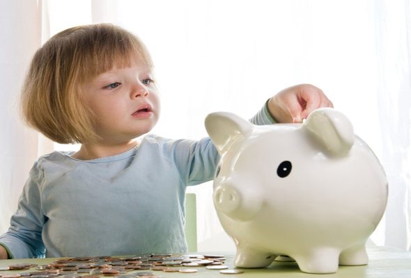 A girl putting coins into a piggy bank.