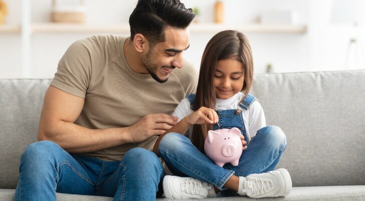 A father and daughter putting coins into a piggy bank.