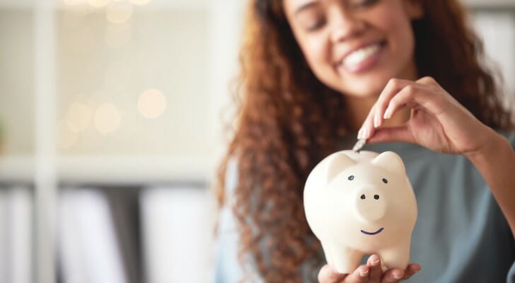 Closeup of a woman putting a coin into a piggy bank.