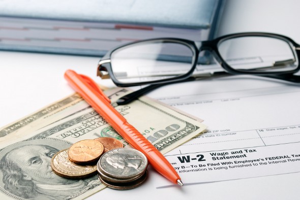 Closeup of a pen, cash and glasses on top of a W-2 form.