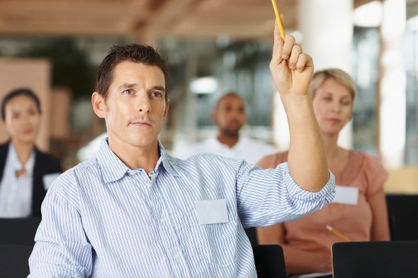 A man, attending a financial literacy class for adults, raises his hand to ask a question on deflation.