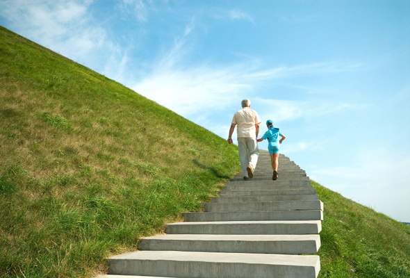A grandparent and grandchild hike up a hill.