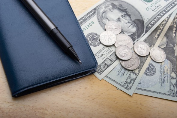 A checkbook and money on a desk.