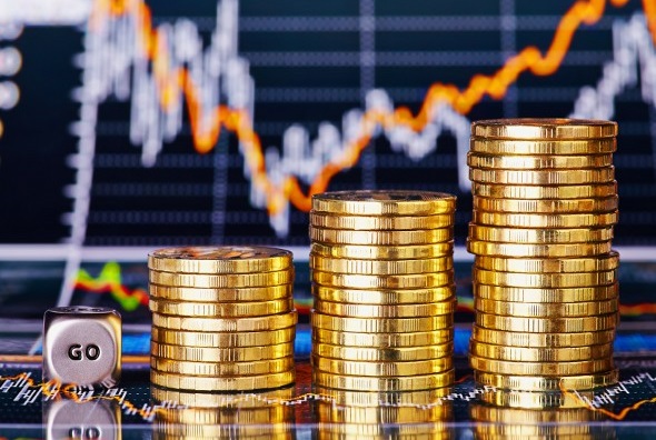 A stack of gold coins in front of a stock chart.