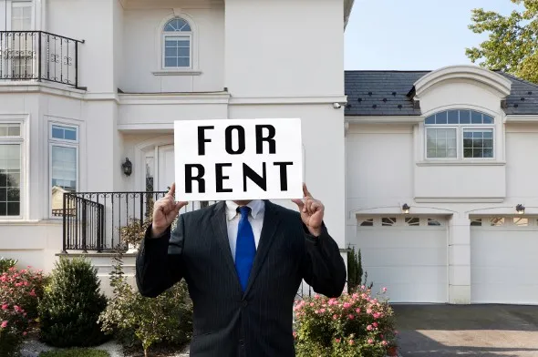 Man holding a "FOR RENT" sign in front of a big house.