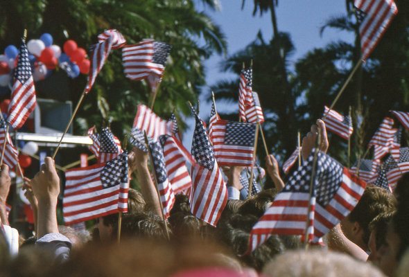 Voters at a campaign rally holding American flags.