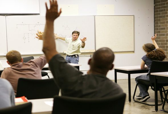 A group of students raise their hands in a classroom.