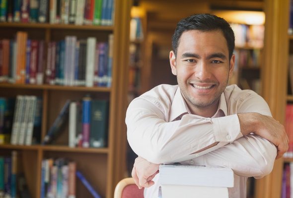 A student leans on a pile of books in the library.