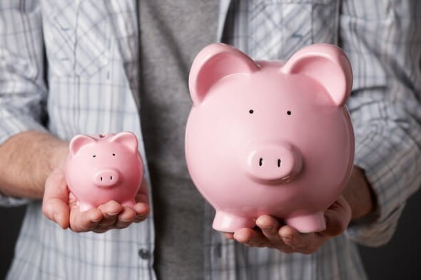 A man holding a small piggy bank in his right hand and a larger one with his left.