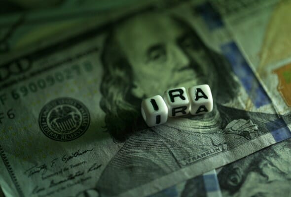 Three dice spelling out "IRA" over a $100 bill.