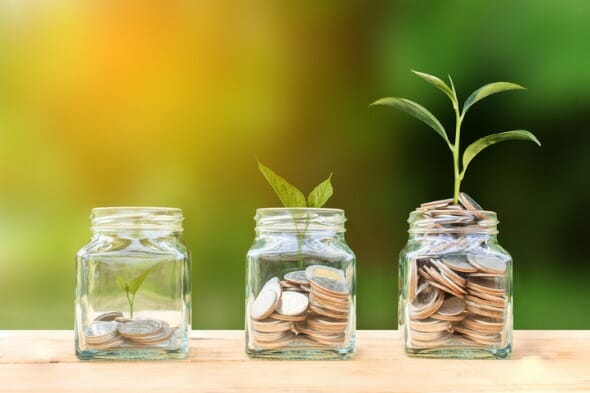 Closeup of three coin jars with a plant growing to represent investment returns.
