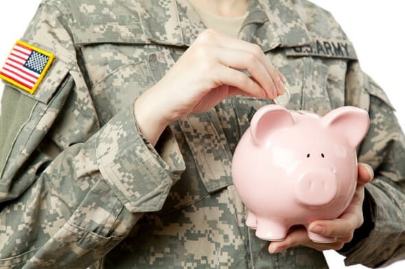 Closeup of a soldier putting money into a piggy bank.