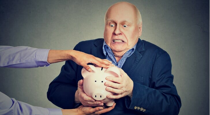 A man holding a piggy bank, as hands reach out to take it.
