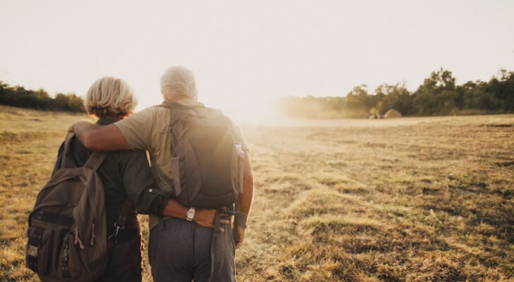 A senior couple walking into the sunset while on a retirement trip.