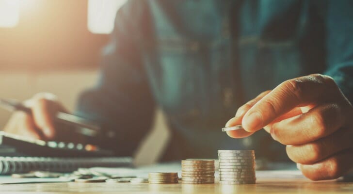 Closeup of a man using a calculator and stacking coins.