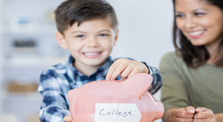 A mother watches her son put money in a piggy bank labeled "college"