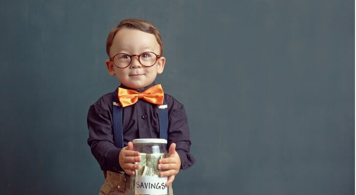 A young child holds a jar labeled "savings."