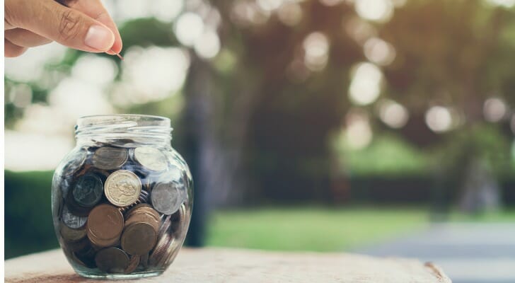 Closeup of a person putting coins into a jar.