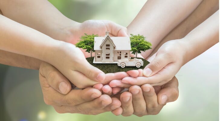 Two sets of hands hold a model house, symbolizing what joint tenancy means for your estate plan.