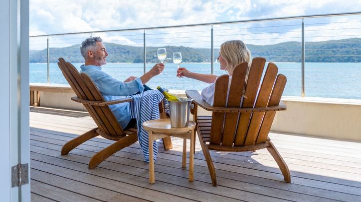 A married couple with a high net worth enjoys a glass of wine together on the deck of a private cruise ship.
