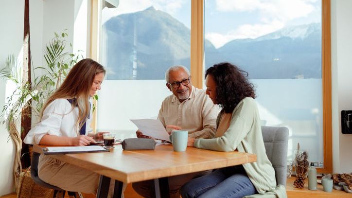 A high-net-worth couple meets with their financial advisor in their home beside a stunning lake.