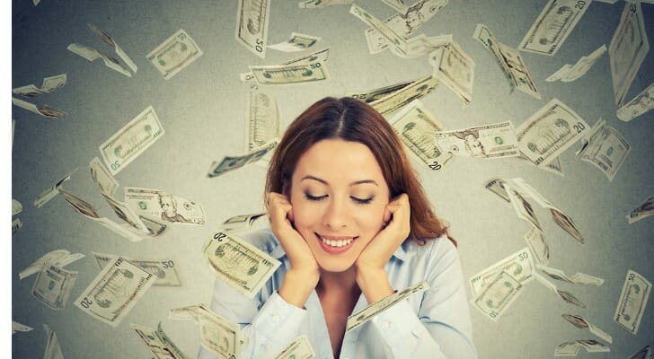 Money being showered down on a happy woman, who is considering how taxes on lottery winnings work.