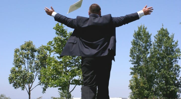 A man in a suit walks away from the camera with his arms raised