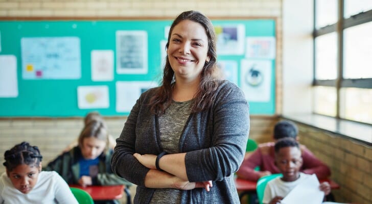 Image shows a female teacher standing in front of a classroom full of students sitting at desks. SmartAsset takes a look at various data sources to complete this year's version of their study on the best U.S. metro areas to be a teacher.