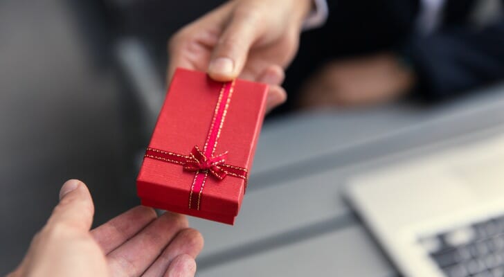 Image shows one person's hand offering a boxed holiday gift to another person's hand. In this study, SmartAsset took a closer look at financial advisors' plans for sending client gifts this year.