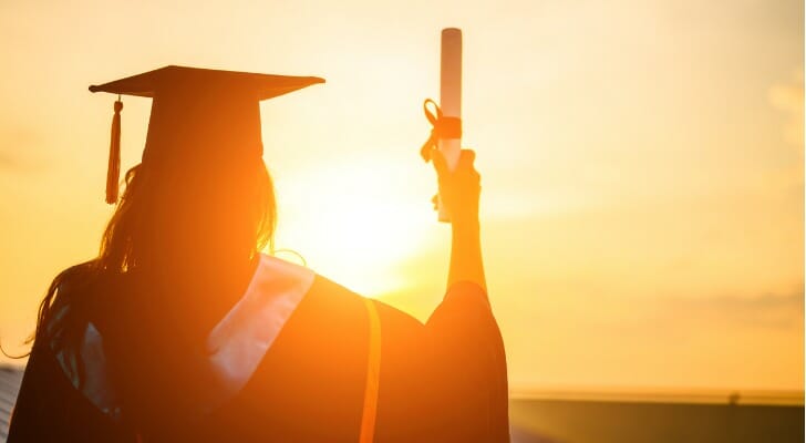 A college graduate holds up a diploma while thinking about pursuing a certification in finance.
