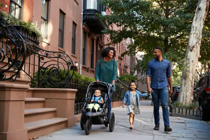Image shows a Black American family walking down a tree-lined street. SmartAsset used data related to income, homeownership and more to determine the cities where Black Americans fared best economically leading up to 2020.