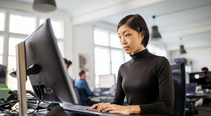Image shows a woman at her desk working at a computer. SmartAsset analyzed various data points to conduct its latest study on the best cities for women in tech.