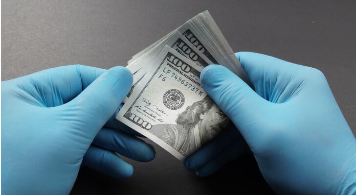 Gloved hands holding a wad of $100 bills