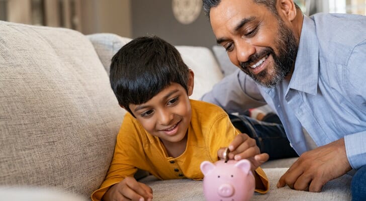 Father and son put money in a piggy bank.