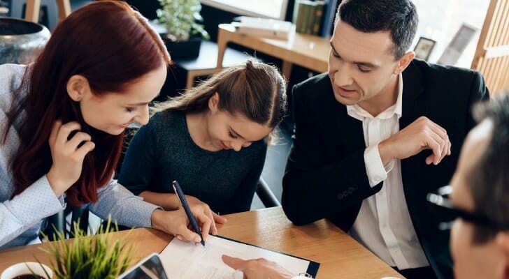 Image shows a young person sitting between two adults, with all three signing a legal document while an attorney looks on.