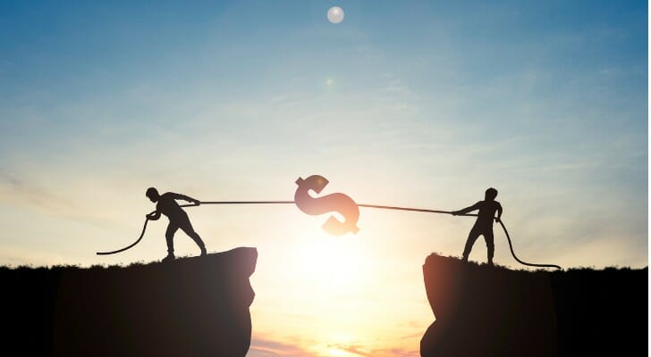 Silhouette of two men pulling a dollar sign between two cliff edges