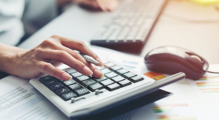 Image shows a financial professional's hand using a calculator to figure average investment management fees.