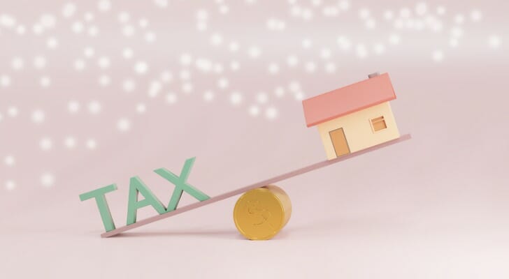 Picture of a house and the word "TAX" on opposite ends of a seesaw