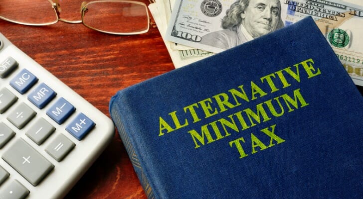 Closeup of a desk with an alternative minimum tax book placed on top of cash.
