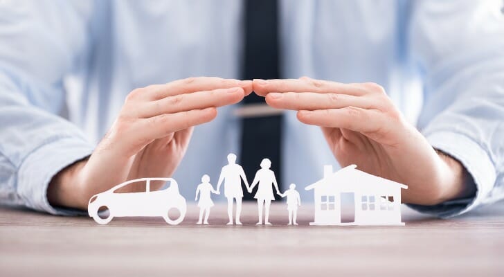 Man's hands held over paper cutouts of a car, a familiy and a house
