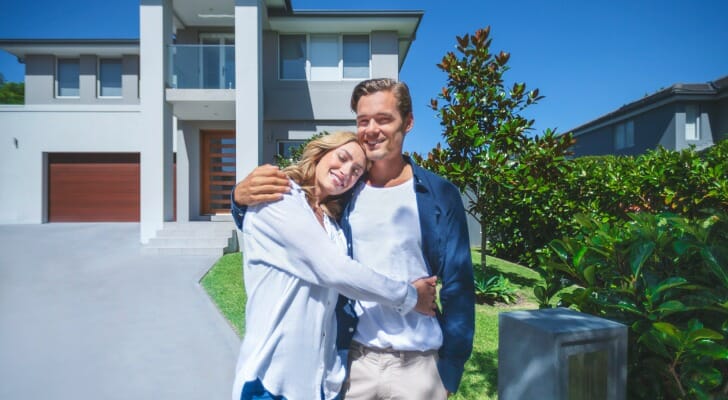A young couple stands outside their new home. SmartAsset compared a 15-year mortgage versus a 30-year mortgage to see which is the better long-term financial decision.
