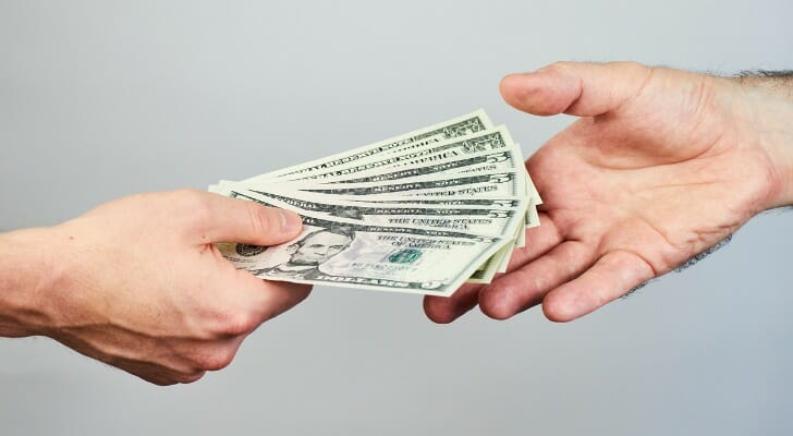 One hand giving cash to another hand.