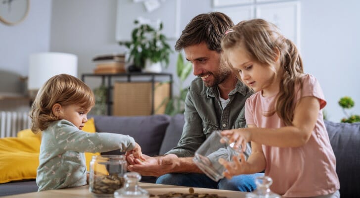 A father using coin jars to teach his daughters about saving.