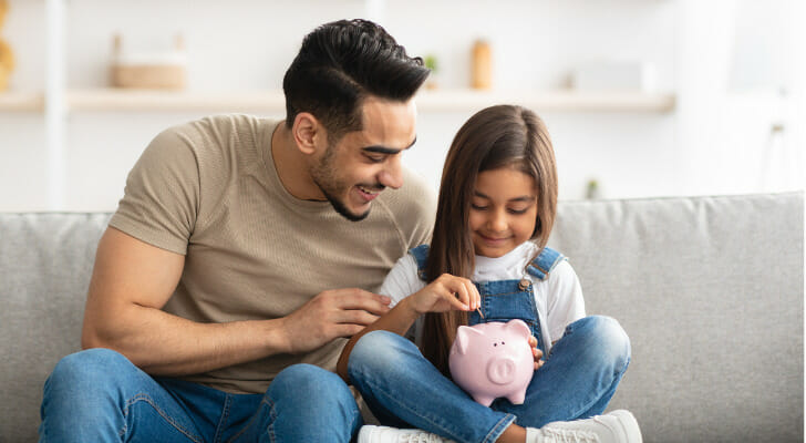 A father teaching his daughter how to save with a piggy bank.