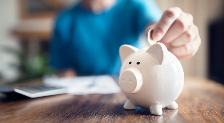 A man putting a coin into a piggy bank.
