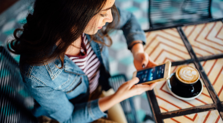 A woman checking her investment account and drinking a cup of coffee.