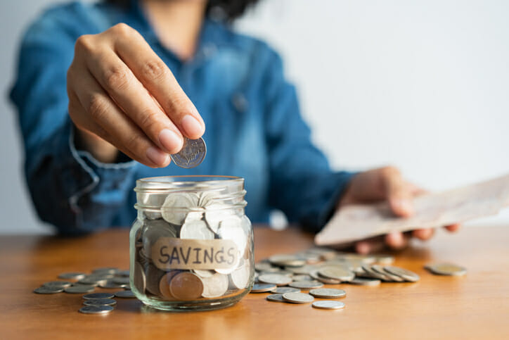 A woman putting coins into a jar to symbolize savings.