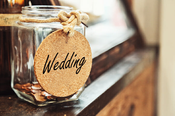 Closeup of a coin jar labeled wedding, representing a wedding savings account.