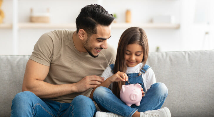 A father and daughter put money in a piggy bank.