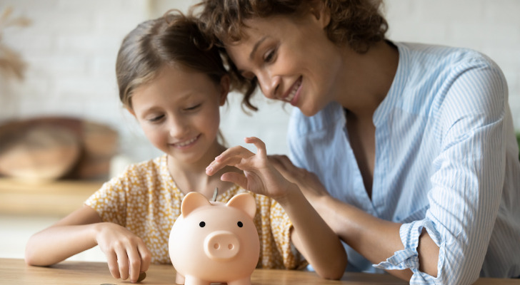 A mother and daughter put money in a piggy bank.